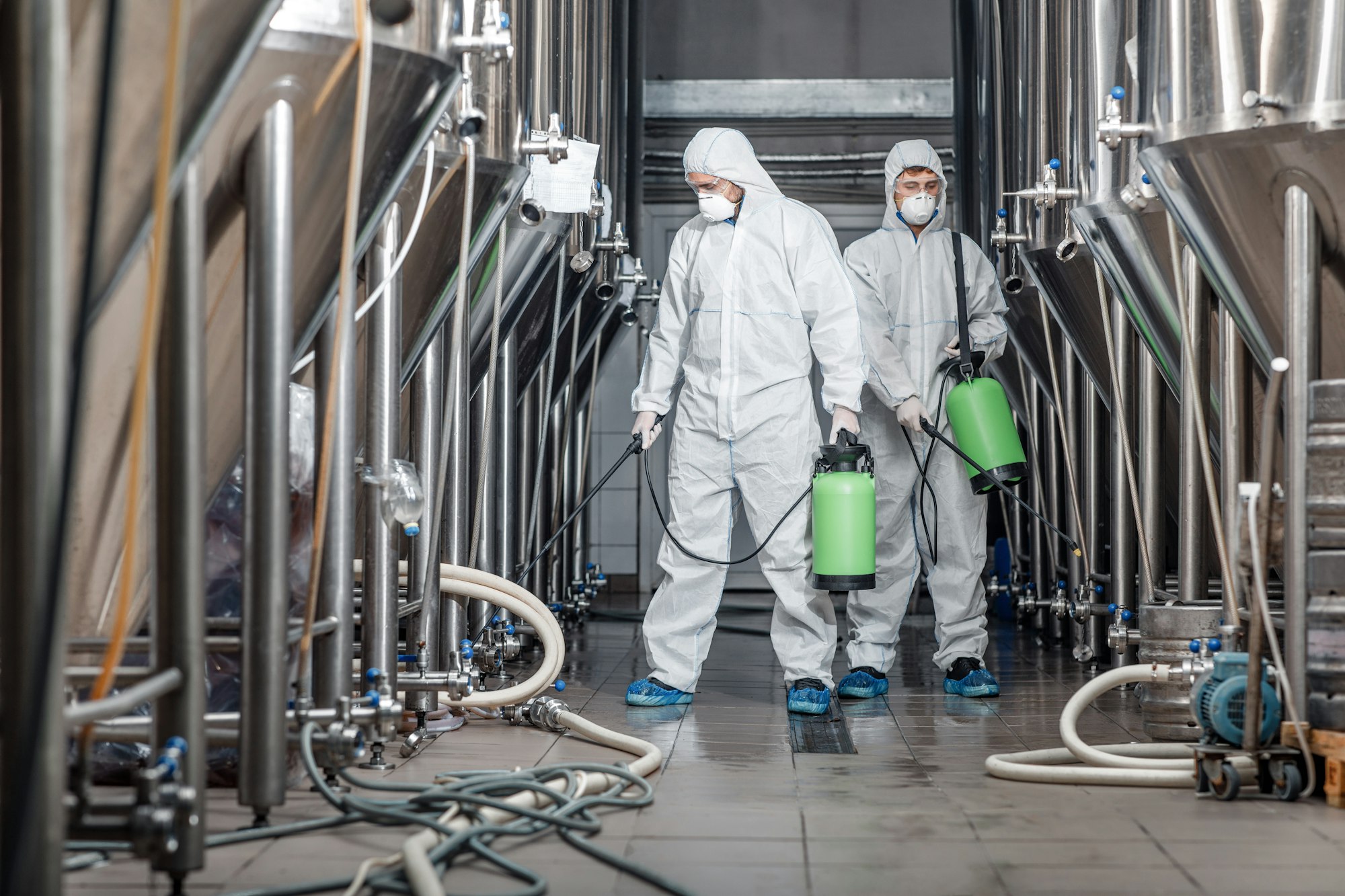 Cleaning and disinfection. Two men in protective suits and spray bag work at plant