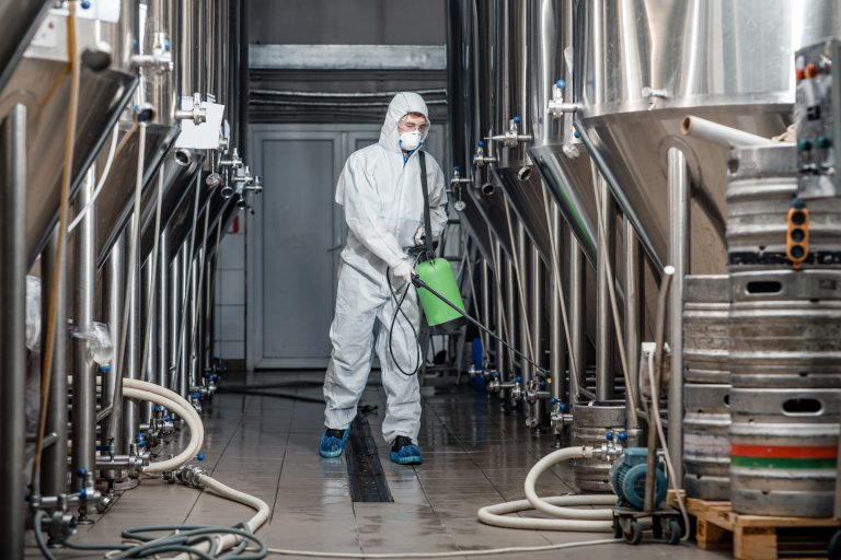 Factory cleaning. Man in protective suit and mask disinfects plant