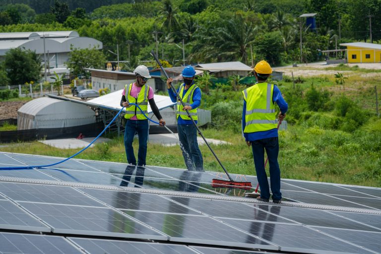 Professional worker cleaning solar panels with brush and water on roof structure.